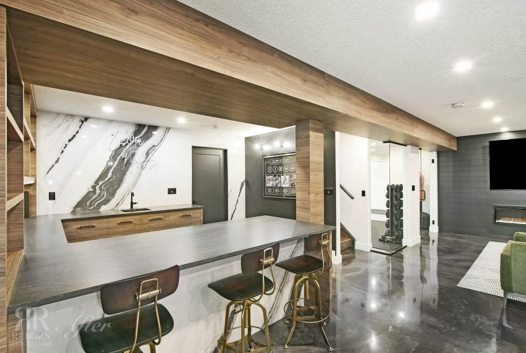 A modern basement bar in the Hamptons area of Calgary with bar stools and a television.