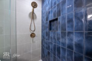 A blue tiled shower with a gold shower head.